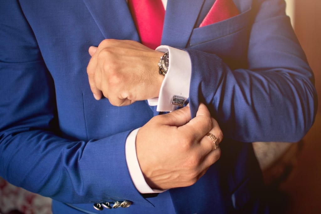 Man accessorizing his suit with a tie, cufflinks, watch, pocket square and ring