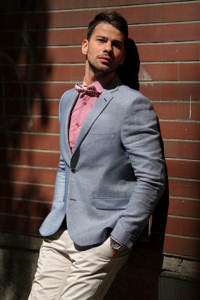 Young man wearing personal uniform leaning on brick wall and posing outdoors.