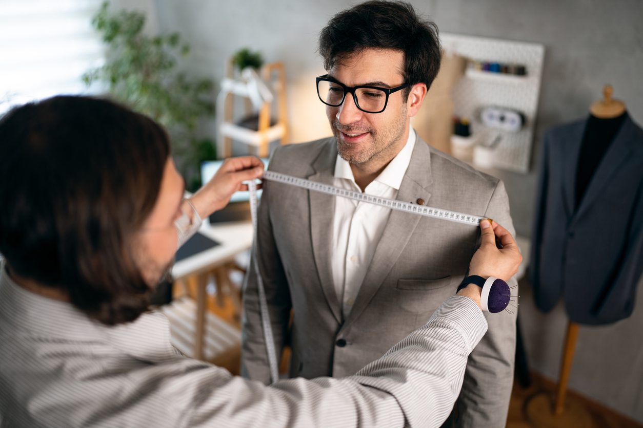 Unrecognizable man measuring a client during a custom-tailoring appointment.