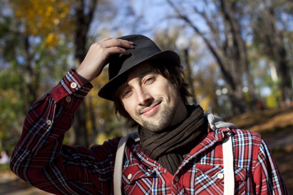 Young man wearing hats while standing in a park.