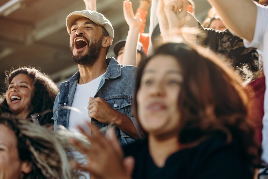 Male fan cheering in the crowd while watching football game.