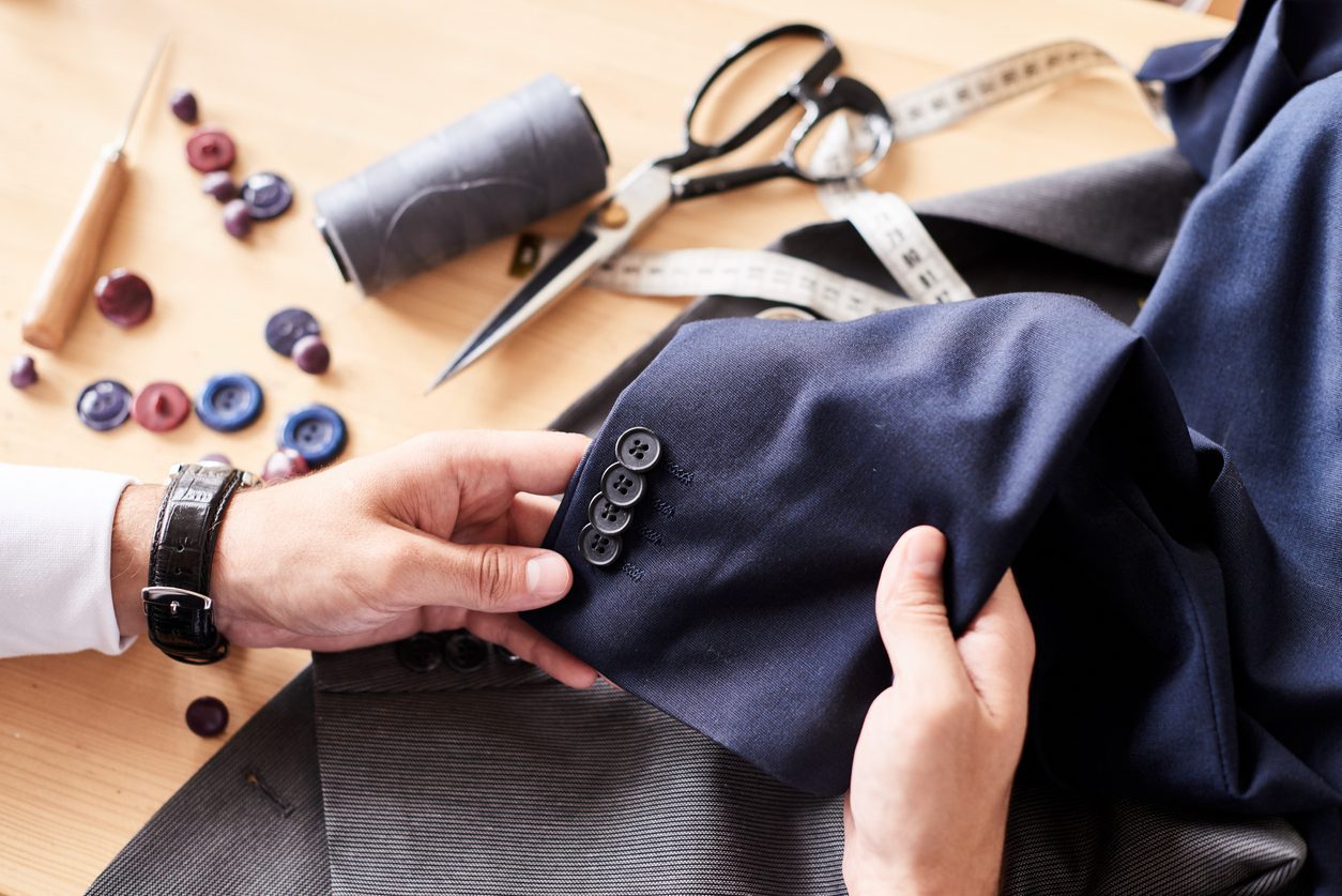 Man's hand repairing custom-tailored clothes on the table.