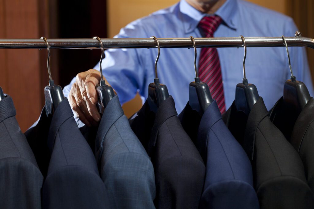 A man’s hand selecting a suit from his professional wardrobe.