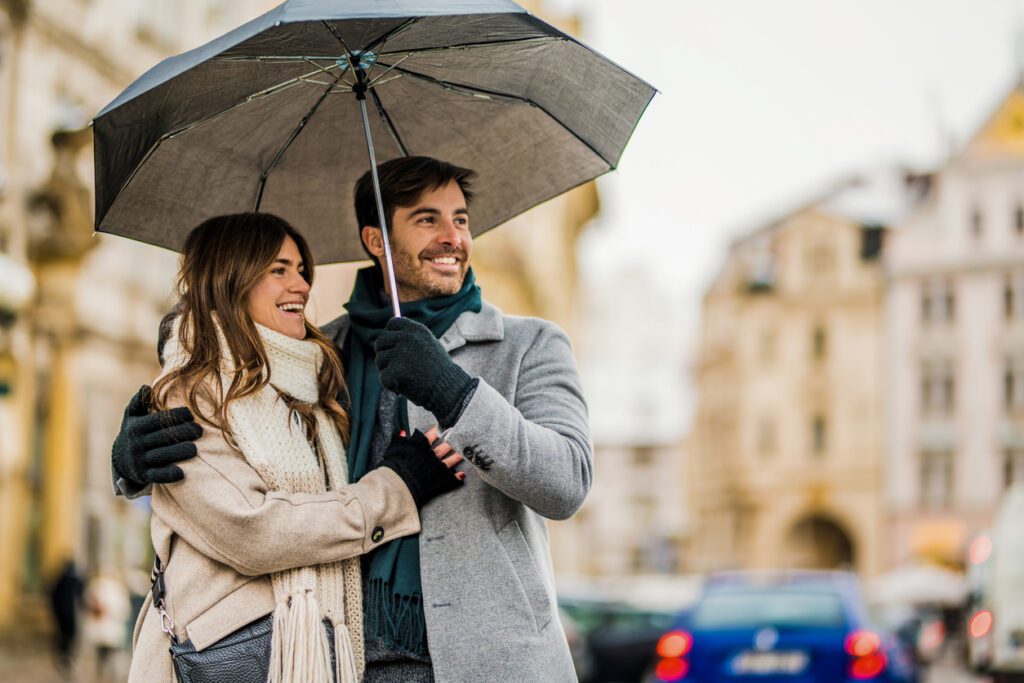 Couple, with rainy-day fashion in mind, walking on city street with an umbrella on a rainy day.