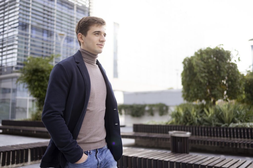 Man wearing transitional outfits confidently standing outside of an office building, looking away in the distance.