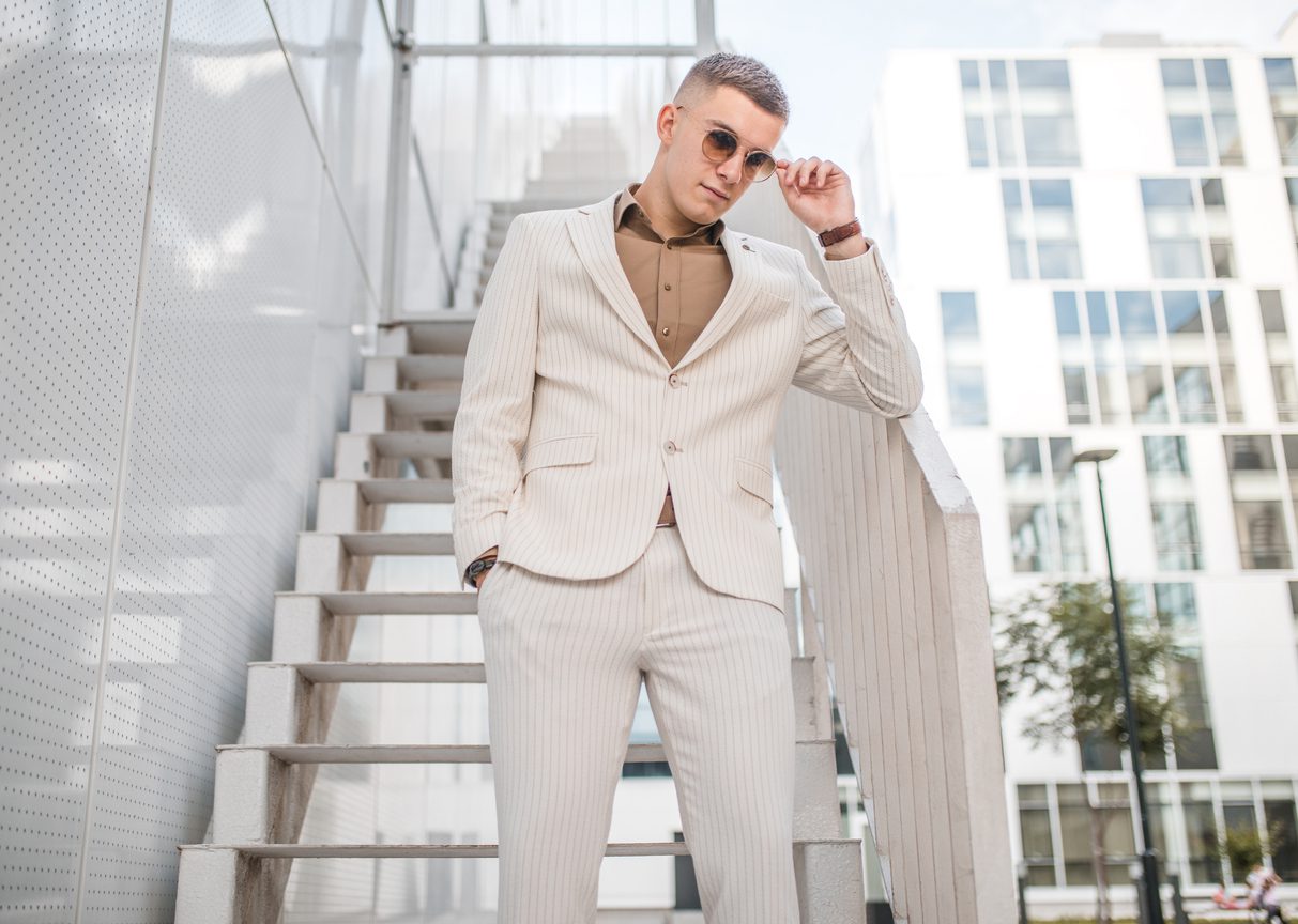 Wan with sunglasses wearing high-end fashion standing on the stairs outdoors.